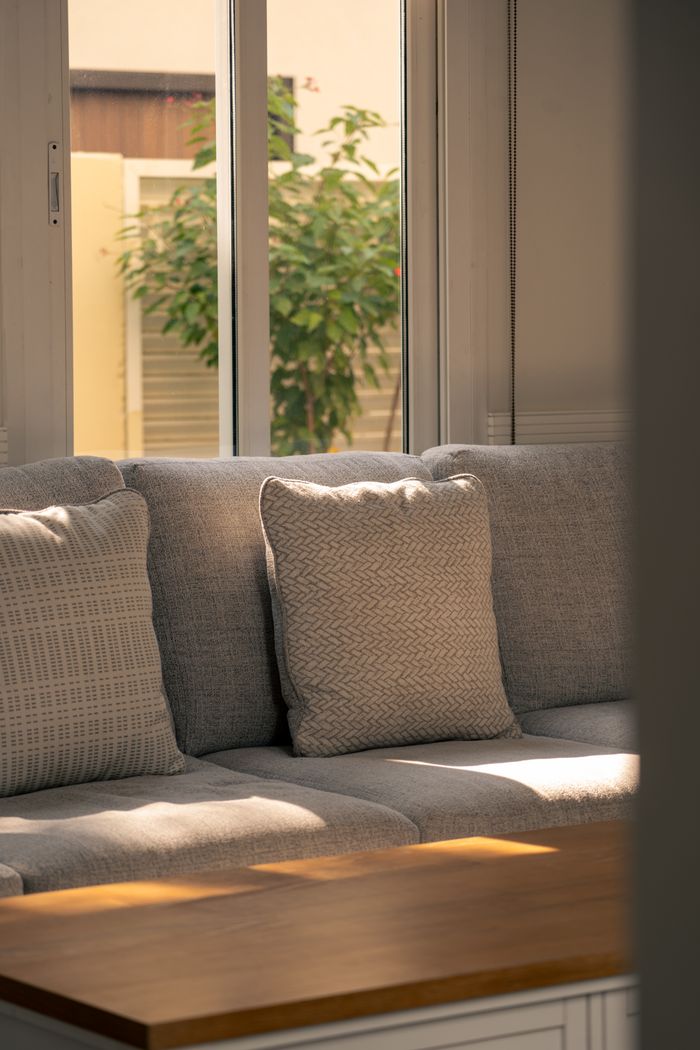 A cozy gray sofa catches warm sunlight by a window in a Dubai home.